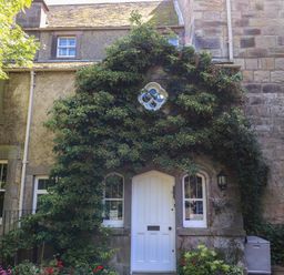 Front view of a stone house with a white door and plants growing around the door at Craster Tower Penthouse in Craster