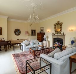 A living room with sofas, a grand piano, framed portraits on walls, a chandelier, a fireplace with a mirror above, and a patterned rug at Craster Tower Penthouse in Craster