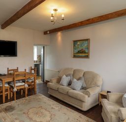 A living room with a dining table and chairs a sofa and armchair a wall-mounted tv and a painting at No2 Budle Bay Cottage in Bamburgh