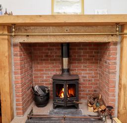 A brick fireplace with a black wood stove and firewood at No2 Budle Bay Cottage in Bamburgh