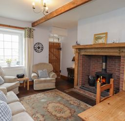 A living room with a fireplace two armchairs a sofa a wooden door and a dining table at No2 Budle Bay Cottage Bamburgh