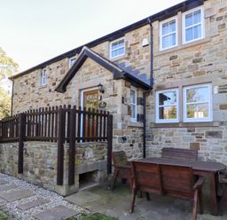 An outdoor seating area with a stone house and wooden furniture at Pippin in Lucker