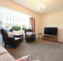 A living room with two black armchairs a sofa a television on a wooden stand and large bay windows at Inveray in Seahouses