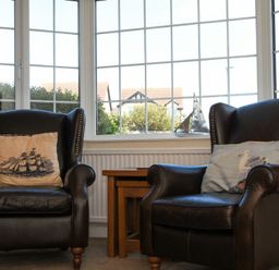 Two leather armchairs with decorative pillows next to a wooden side table in front of large windows at Inveray in Seahouses