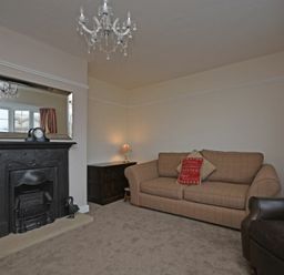 A living room with a brown sofa a black fireplace a mirror and a chandelier at Inveray in Seahouses