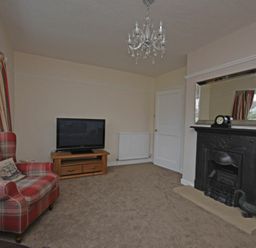 A living room with a fireplace a TV on a wooden stand and a plaid armchair at Inveray in Seahouses
