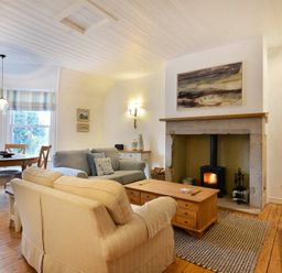 A living room with a wood stove in a stone fireplace a wooden coffee table two sofas a dining table with chairs and a television at Periwinkle in Bamburgh