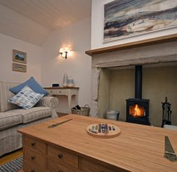 A living room with a striped sofa and cushions a wooden table with a game a fireplace with a fire and painting above at Periwinkle in Bamburgh