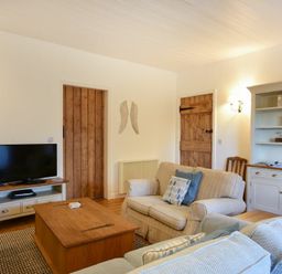 A living room with a television on a stand a wooden coffee table two sofas and a cabinet at Periwinkle in Bamburgh