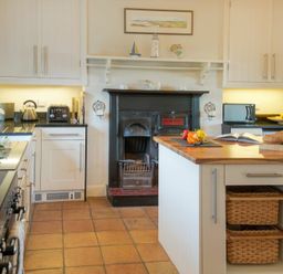 A kitchen with a wooden island countertop and baskets underneath a fireplace with white cabinets at The Villas No3 in Embleton