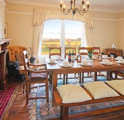 A dining room with wooden table and chairs a fireplace armchair and large window at The Villas No3 in Embleton