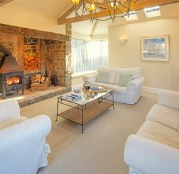 A living room with white sofas a stone fireplace and a glass coffee table at The Villas No3 in Embleton