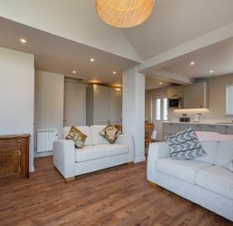 An open living room and kitchen with two beige sofas and wooden flooring at Castle View Bamburgh