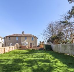 A backyard with green grass fenced by wooden panels and a house with a conservatory at St Marys Cottages No1 in Low Newton-by-the-Sea