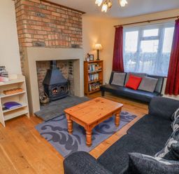 A living room with a wood burning stove brick fireplace wooden coffee table and two sofas at St Marys Cottages No1 in Low Newton-by-the-Sea