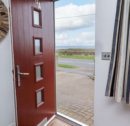 A hallway with a red door and a mirror at Farne Cottage Beadnell