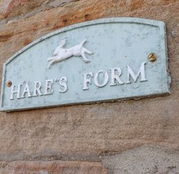A wall-mounted sign with a hare figure and the text Hares Form on a stone wall at Hares Form in Seahouses