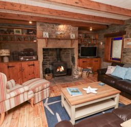 A living room with stone walls wooden beams a fireplace armchair and leather sofas at Hares Form in Seahouses