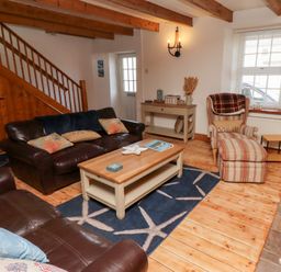 A living room with brown leather sofas a striped armchair with ottoman wooden coffee table and a staircase at Hares Form in Seahouses