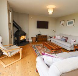 A living room with a wood burning stove wooden floors sofas a wooden coffee table and a wall mounted television at The Mustard Pot in Acklington