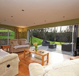 A living room with sofas and a coffee table opening to a patio with outdoor chairs at Quarry Haven in Bamburgh