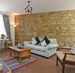 A living room with a stone wall a sofa armchair coffee table and small dining table at Sea Air in Amble