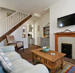 A living room with a sofa armchair wooden coffee table fireplace and stairs at Sea Air in Amble