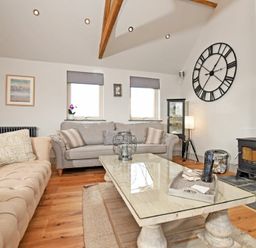 A living room with two sofas a coffee table a wood burning stove and a large wall clock at The Hemmel (Beadnell) in Beadnell