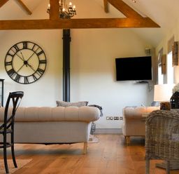 A living room with two beige sofas a black chair a wicker chair a wall clock a wall mounted television and exposed wooden beams at The Hemmel Beadnell