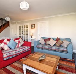 A living room with two sofas a wooden coffee table and a staircase at Armstrong Cottages No22 in Bamburgh