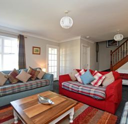 A living room with two sofas a wooden coffee table and a staircase at Armstrong Cottages No22 Bamburgh