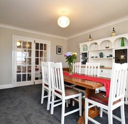 A dining room with a wooden table and white chairs with a red runner and flowers at Armstrong Cottages No22 in Bamburgh