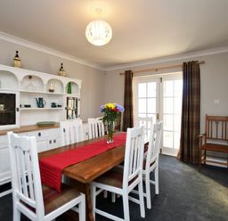 A dining room with a wooden table and white chairs and a white cabinet with dishes at Armstrong Cottages No22 Bamburgh