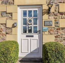 An entrance with a front door and bush at Dunlin Cottage in Bamburgh