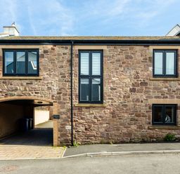 A stone building with black framed windows and an archway driveway at Harbour Lights House in Seahouses