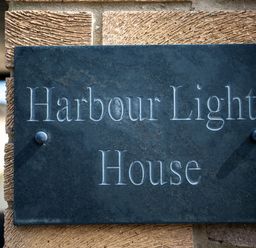 A sign with the text Harbour Lights House mounted on a stone wall at Harbour Lights House in Seahouses