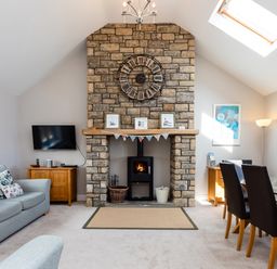 A living room with a stone fireplace a clock above and a sofa and dining table at Harbour Lights House in Seahouses