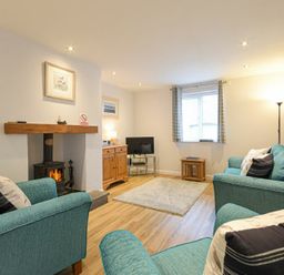 A living room with teal sofas a wood burning stove and television at Braidcarr Cottage in Seahouses