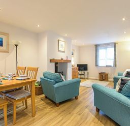 A living room with blue sofas a dining table with chairs a television and a window with curtains at Braidcarr Cottage in Seahouses