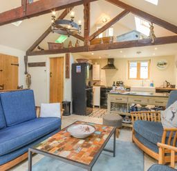 A living room with blue sofas a wooden coffee table and an open kitchen at The Byre at Warkworth