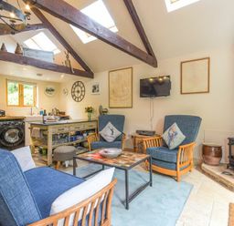 A seating area with blue armchairs and a coffee table next to a kitchen and wood burning stove at The Byre at Warkworth