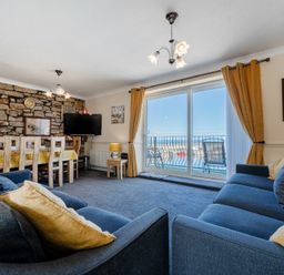 A living room with blue sofas a dining table and sliding glass doors leading to a balcony at Lobster Lodge in Seahouses