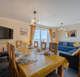 A dining and living room with a yellow tablecloth on the table and blue sofas at Lobster Lodge in Seahouses