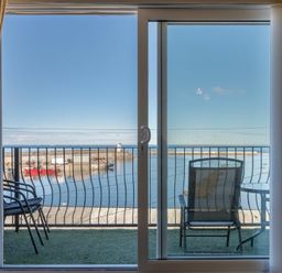 View through sliding glass doors to a balcony with chairs and table overlooking a harbor at Lobster Lodge in Seahouses