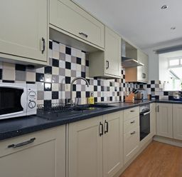 A kitchen with beige cabinets a microwave oven dish rack stove oven and window with plant at East Havers in Alnwick