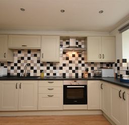 A kitchen with cream cabinets black and white checkered backsplash stove microwave and various kitchen appliances at East Havers in Alnwick
