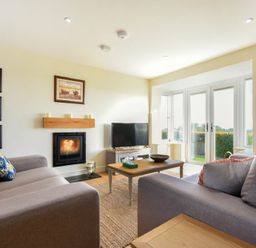 A living room with two sofas a coffee table a TV and a fireplace near glass doors at Rock Lodge in Alnmouth