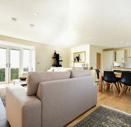 A living room with sofas a dining table and chairs next to a kitchen with white cabinets at Rock Lodge in Alnmouth