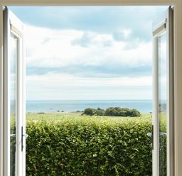 A view through open doors showing a hedge green fields trees and the sea at Rock Lodge in Alnmouth