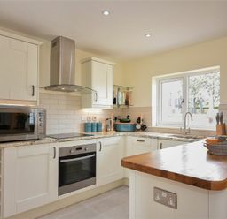 A kitchen with white cabinets a microwave an oven a stovetop and a wooden countertop at Rock Lodge in Alnmouth